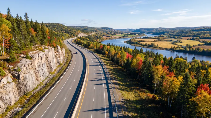 Illustration générée : une autoroute à quatre voies longe une paroi de granit et traverse des collines boisées aux couleurs d'automne, au-dessus d'une rivière.